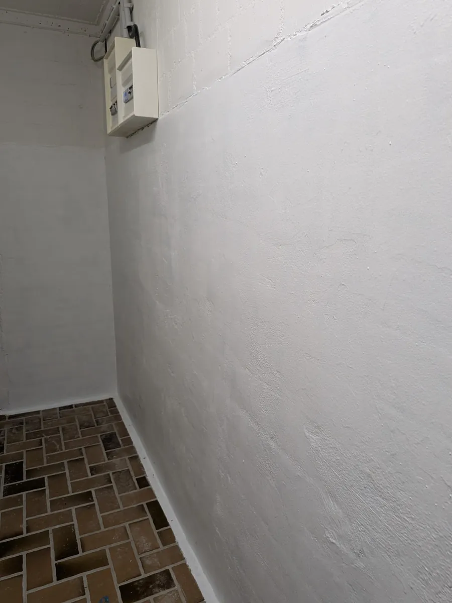 Fertig abgedichtete und weiß beschichtete Kellerwand über einem Ziegelboden